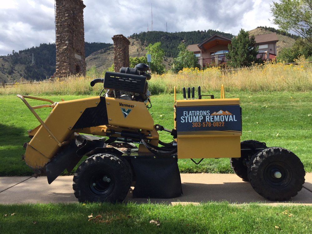 The yellow Vermeer stump grinder parked on a sidewalk with foothills behind it