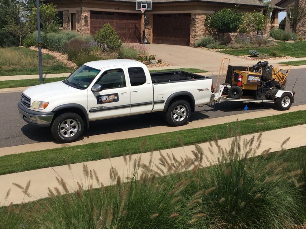 White Toyota pickup towing the stump grinder on a small trailer in front of a house